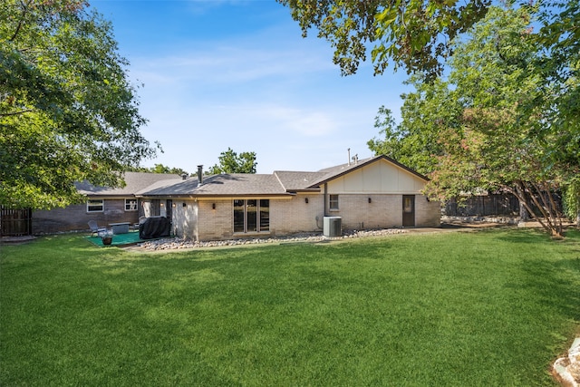 rear view of house with central AC unit and a lawn