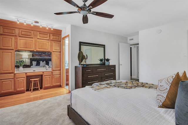 bedroom with ceiling fan, light hardwood / wood-style flooring, built in desk, track lighting, and ensuite bathroom