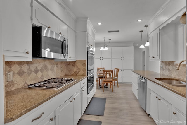 kitchen with hanging light fixtures, stainless steel appliances, sink, light wood-type flooring, and white cabinets