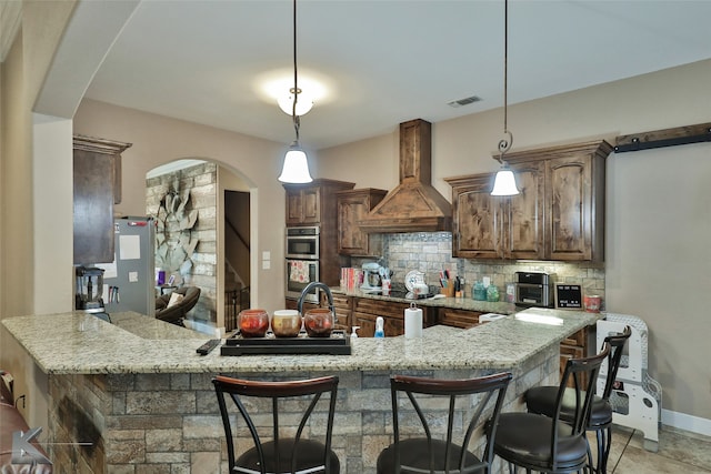 kitchen with light stone counters, stainless steel double oven, custom exhaust hood, decorative backsplash, and black electric cooktop