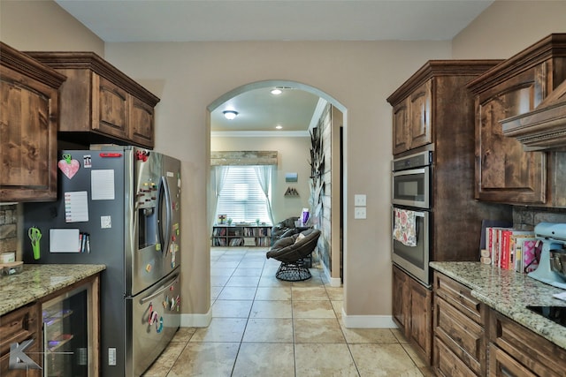 kitchen featuring crown molding, dark brown cabinetry, stainless steel appliances, and light stone counters