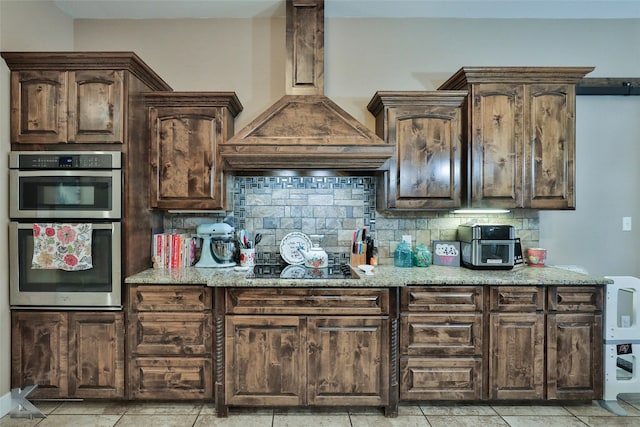 kitchen featuring custom range hood, backsplash, dark brown cabinets, and light tile patterned floors