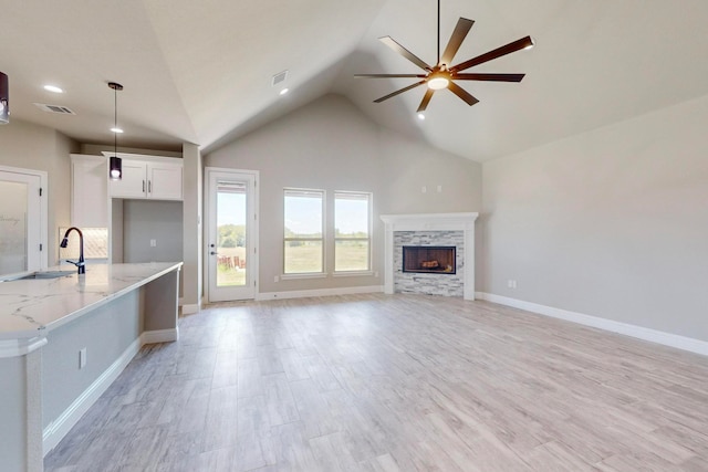 unfurnished living room featuring high vaulted ceiling, a stone fireplace, ceiling fan, light hardwood / wood-style flooring, and sink