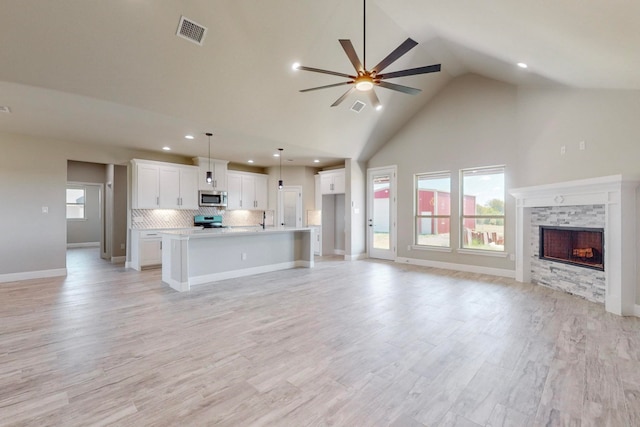 unfurnished living room featuring light wood-type flooring, a stone fireplace, ceiling fan, and high vaulted ceiling