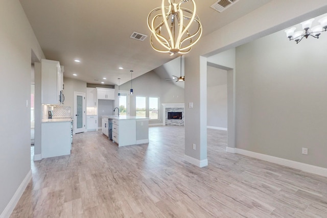 kitchen featuring white cabinets, a stone fireplace, a kitchen island with sink, light hardwood / wood-style flooring, and ceiling fan with notable chandelier