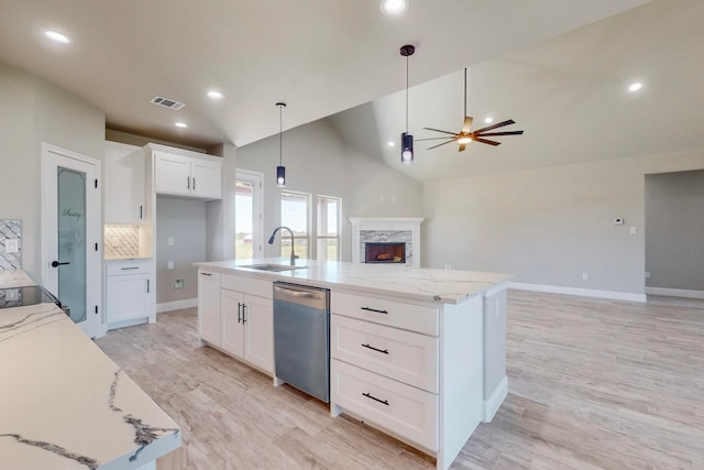 kitchen with ceiling fan, a stone fireplace, dishwasher, and a center island with sink