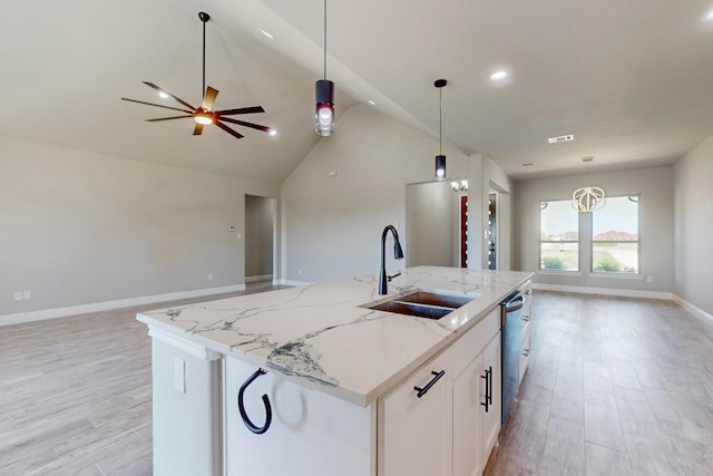 kitchen with light stone counters, a center island with sink, hanging light fixtures, and ceiling fan