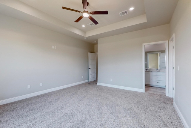 unfurnished bedroom featuring ceiling fan, connected bathroom, sink, a tray ceiling, and light carpet