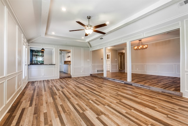 unfurnished living room with ceiling fan with notable chandelier, a raised ceiling, ornamental molding, and hardwood / wood-style flooring