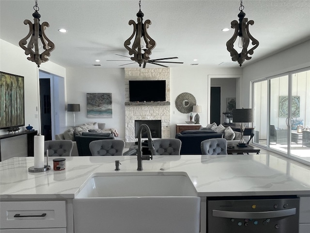 kitchen with light stone counters, decorative light fixtures, dishwasher, a center island, and a stone fireplace