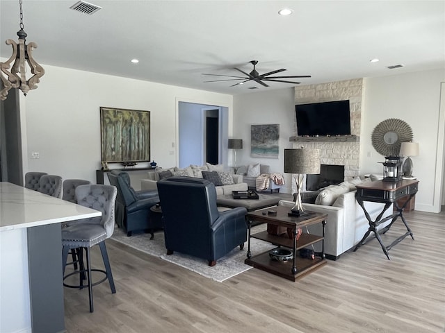 living room featuring ceiling fan, a stone fireplace, and light wood-type flooring