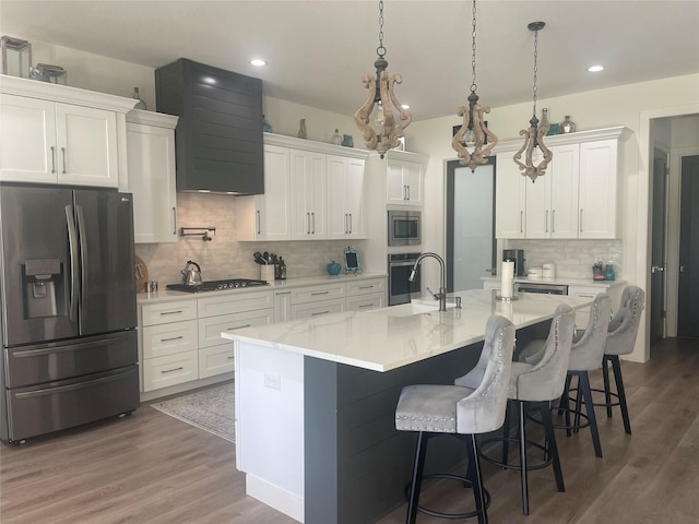 kitchen with sink, white cabinetry, stainless steel appliances, and an island with sink