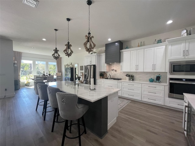 kitchen featuring a kitchen island with sink, white cabinets, hanging light fixtures, dark hardwood / wood-style floors, and appliances with stainless steel finishes