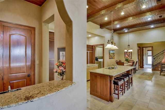 kitchen featuring light stone countertops, sink, wooden ceiling, decorative light fixtures, and a kitchen island with sink