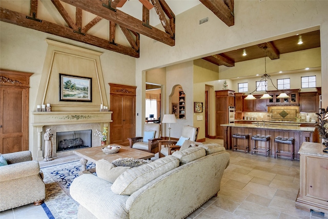 living room featuring beamed ceiling, plenty of natural light, high vaulted ceiling, and a tiled fireplace