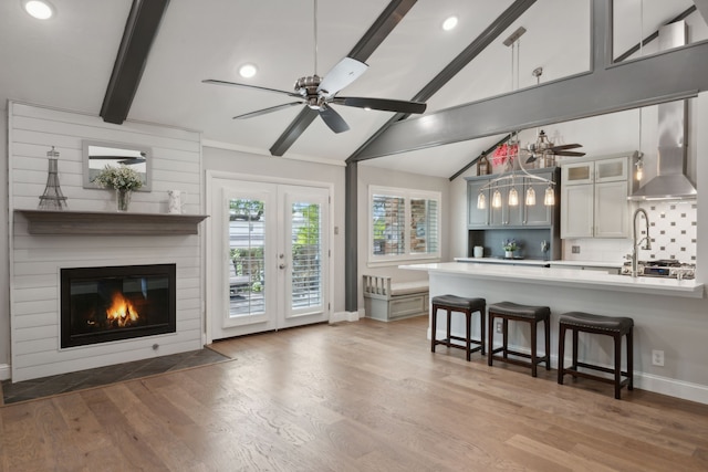 kitchen featuring pendant lighting, hardwood / wood-style flooring, ceiling fan, a kitchen breakfast bar, and wall chimney exhaust hood