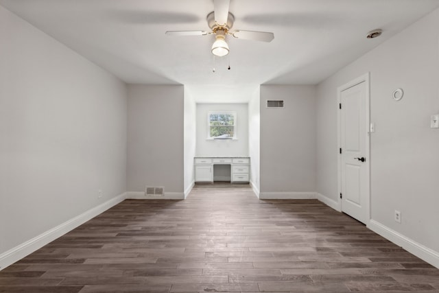 unfurnished living room with ceiling fan, dark hardwood / wood-style flooring, and built in desk