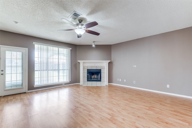 unfurnished living room featuring ceiling fan, a textured ceiling, light hardwood / wood-style flooring, and a tiled fireplace