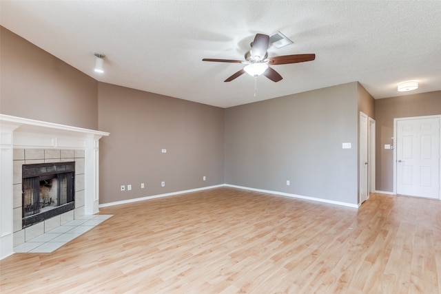 unfurnished living room featuring light wood-type flooring, a tile fireplace, a textured ceiling, and ceiling fan