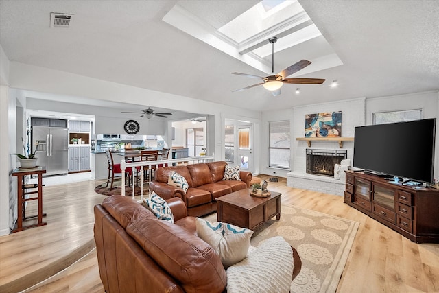 living room featuring light hardwood / wood-style floors, ceiling fan, a brick fireplace, and plenty of natural light