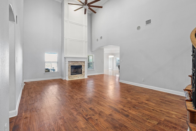 unfurnished living room featuring ceiling fan, a stone fireplace, a high ceiling, and wood-type flooring