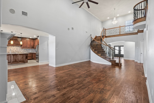 unfurnished living room featuring ceiling fan with notable chandelier, light wood-type flooring, a high ceiling, and ornamental molding