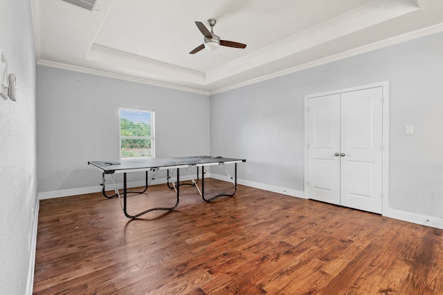 game room with ceiling fan, a tray ceiling, dark hardwood / wood-style floors, and ornamental molding