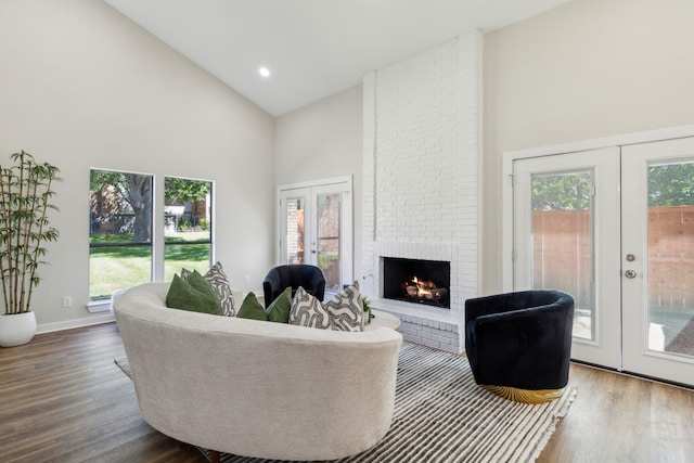 living room with high vaulted ceiling, a brick fireplace, hardwood / wood-style floors, and french doors