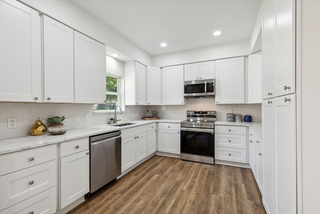 kitchen with white cabinetry, dark wood-type flooring, light stone counters, stainless steel appliances, and sink