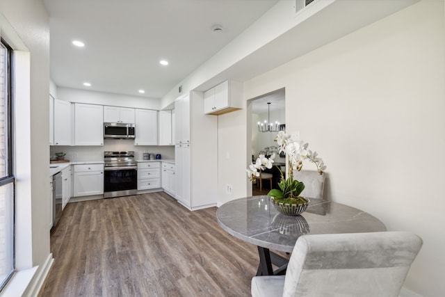 kitchen featuring light wood-type flooring, a chandelier, white cabinets, hanging light fixtures, and appliances with stainless steel finishes