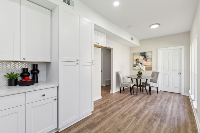 kitchen featuring decorative backsplash, white cabinets, hardwood / wood-style flooring, and light stone countertops