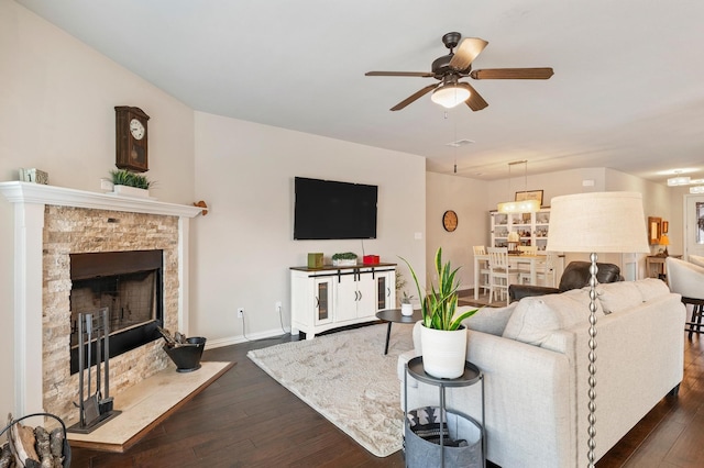 living room with a stone fireplace, dark hardwood / wood-style flooring, and ceiling fan