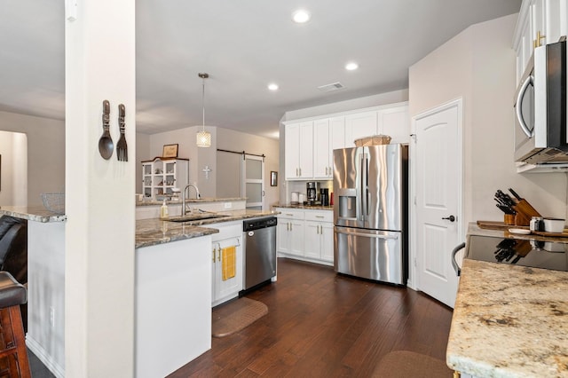 kitchen with white cabinets, sink, decorative light fixtures, appliances with stainless steel finishes, and a barn door