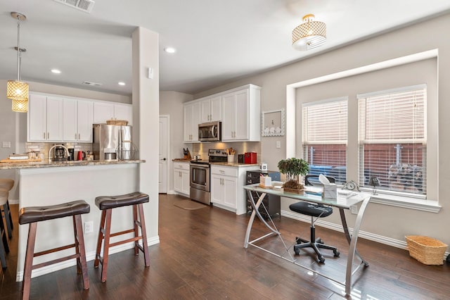 kitchen with appliances with stainless steel finishes, hanging light fixtures, white cabinetry, light stone counters, and dark hardwood / wood-style flooring