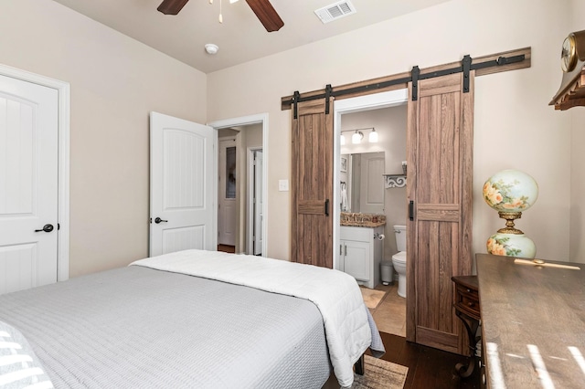 bedroom featuring connected bathroom, ceiling fan, wood-type flooring, and a barn door