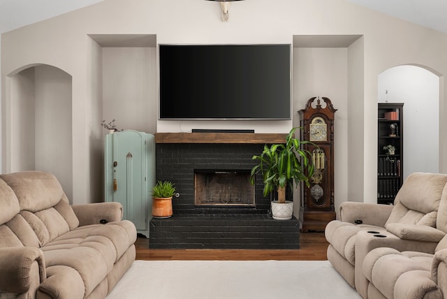 living room featuring wood-type flooring, vaulted ceiling, and a brick fireplace