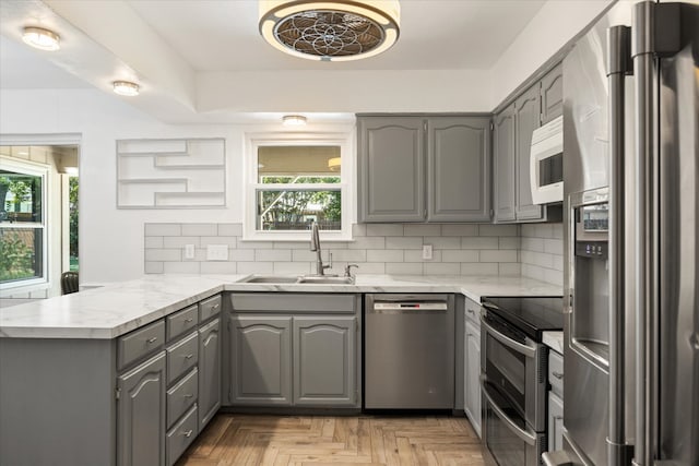 kitchen featuring gray cabinets, sink, kitchen peninsula, decorative backsplash, and stainless steel appliances