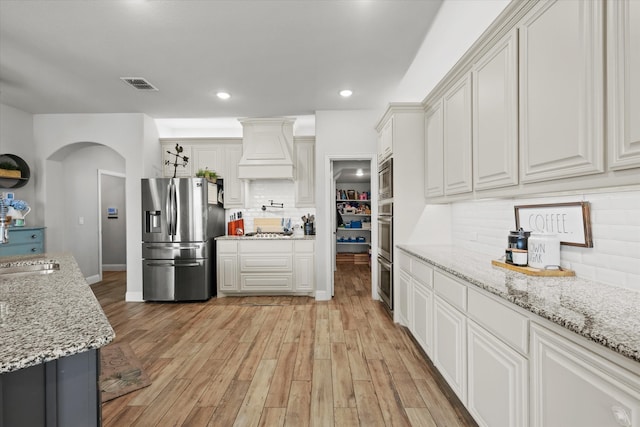 kitchen featuring light stone counters, white cabinets, tasteful backsplash, light hardwood / wood-style flooring, and stainless steel appliances