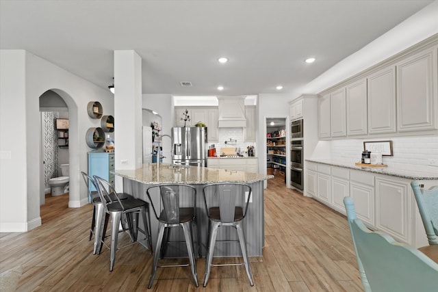 kitchen featuring light hardwood / wood-style flooring, decorative backsplash, appliances with stainless steel finishes, and custom exhaust hood