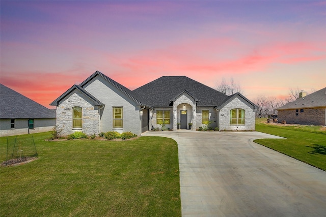 french provincial home with roof with shingles, a front lawn, concrete driveway, and stone siding