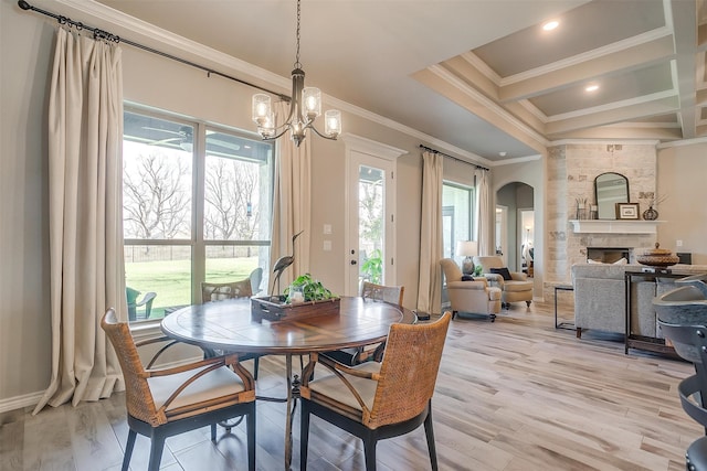 dining space with a healthy amount of sunlight, a stone fireplace, ornamental molding, and light hardwood / wood-style flooring