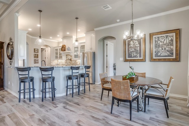 dining space with light wood-type flooring, crown molding, and a chandelier