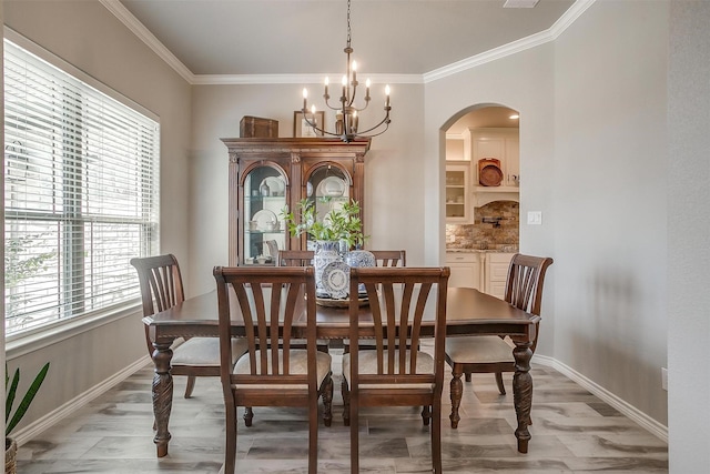 dining space with light wood finished floors, a chandelier, baseboards, ornamental molding, and arched walkways