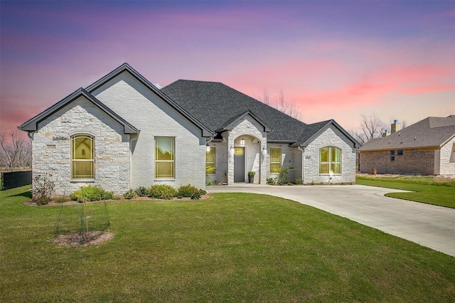french country inspired facade featuring a yard, concrete driveway, and stone siding