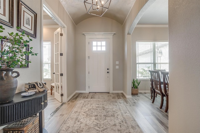 foyer entrance with an inviting chandelier, lofted ceiling, light hardwood / wood-style floors, and ornamental molding