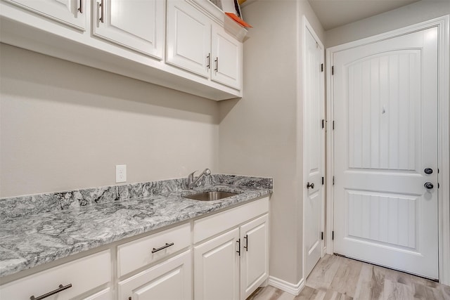 kitchen with light hardwood / wood-style floors, sink, light stone counters, and white cabinets