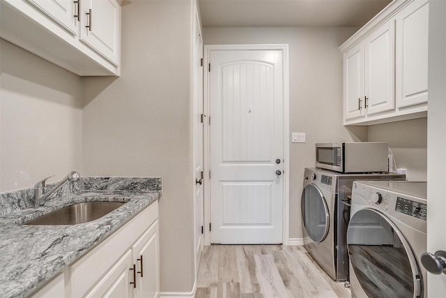 clothes washing area with washer and dryer, light wood-style floors, cabinet space, a sink, and baseboards