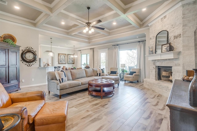 living area featuring a ceiling fan, light wood-style floors, a stone fireplace, and crown molding