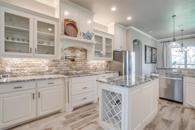 kitchen featuring crown molding, backsplash, white cabinetry, arched walkways, and appliances with stainless steel finishes