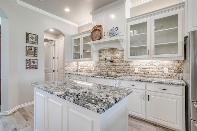 kitchen featuring arched walkways, black electric stovetop, decorative backsplash, white cabinetry, and crown molding